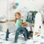 The image shows a little girl sitting in a high chair, smiling and playing with a toy. She is surrounded by a variety of books and toys, which are placed on a table in front of her. The girl appears to be enjoying her time and is engaged in her playtime activities.