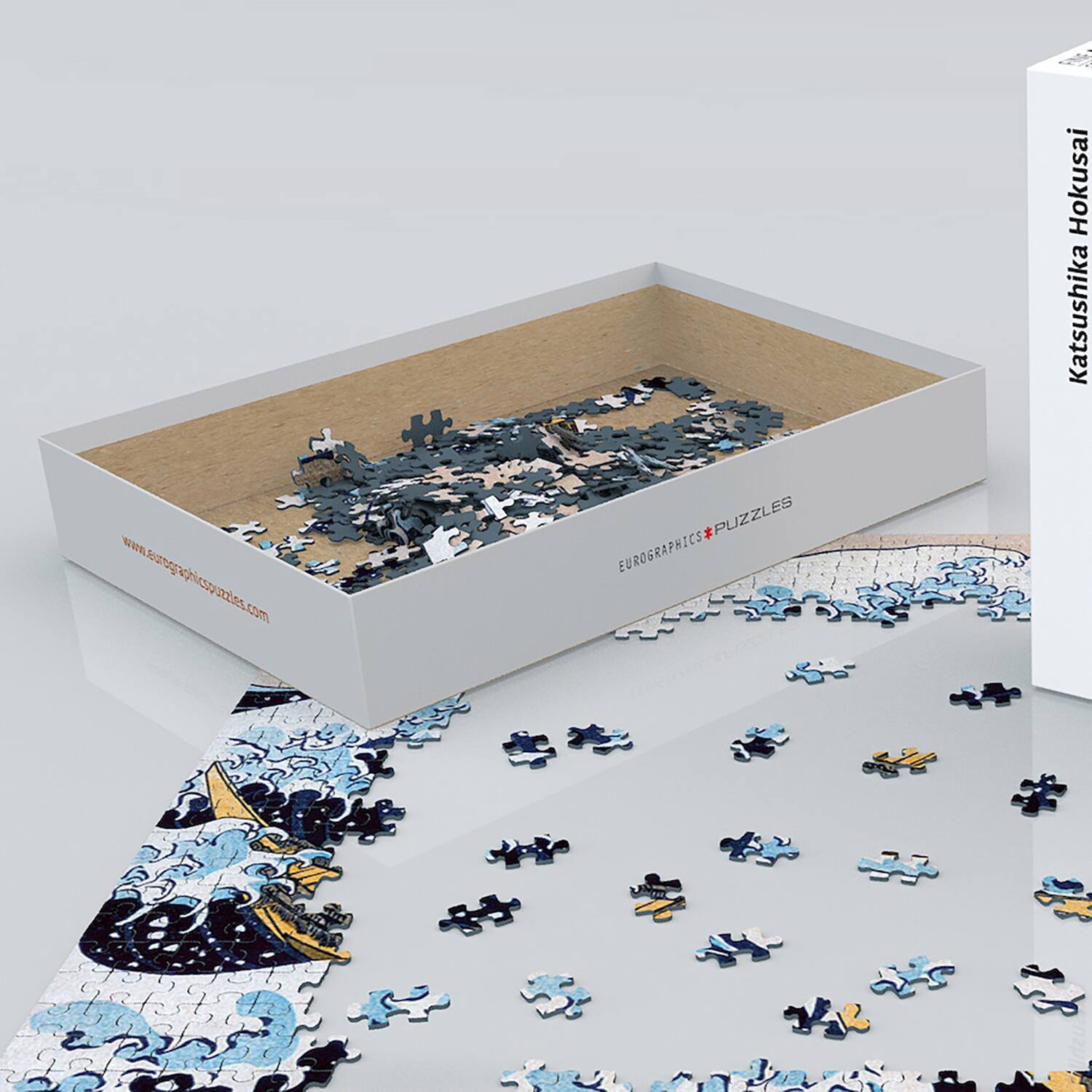 The image features a box of puzzles by Hokusai Katsushika. The puzzles are made by Eurographics and are designed with a blue and black color scheme. The puzzle pieces are scattered around the box, showcasing the intricate designs and patterns of the puzzles.