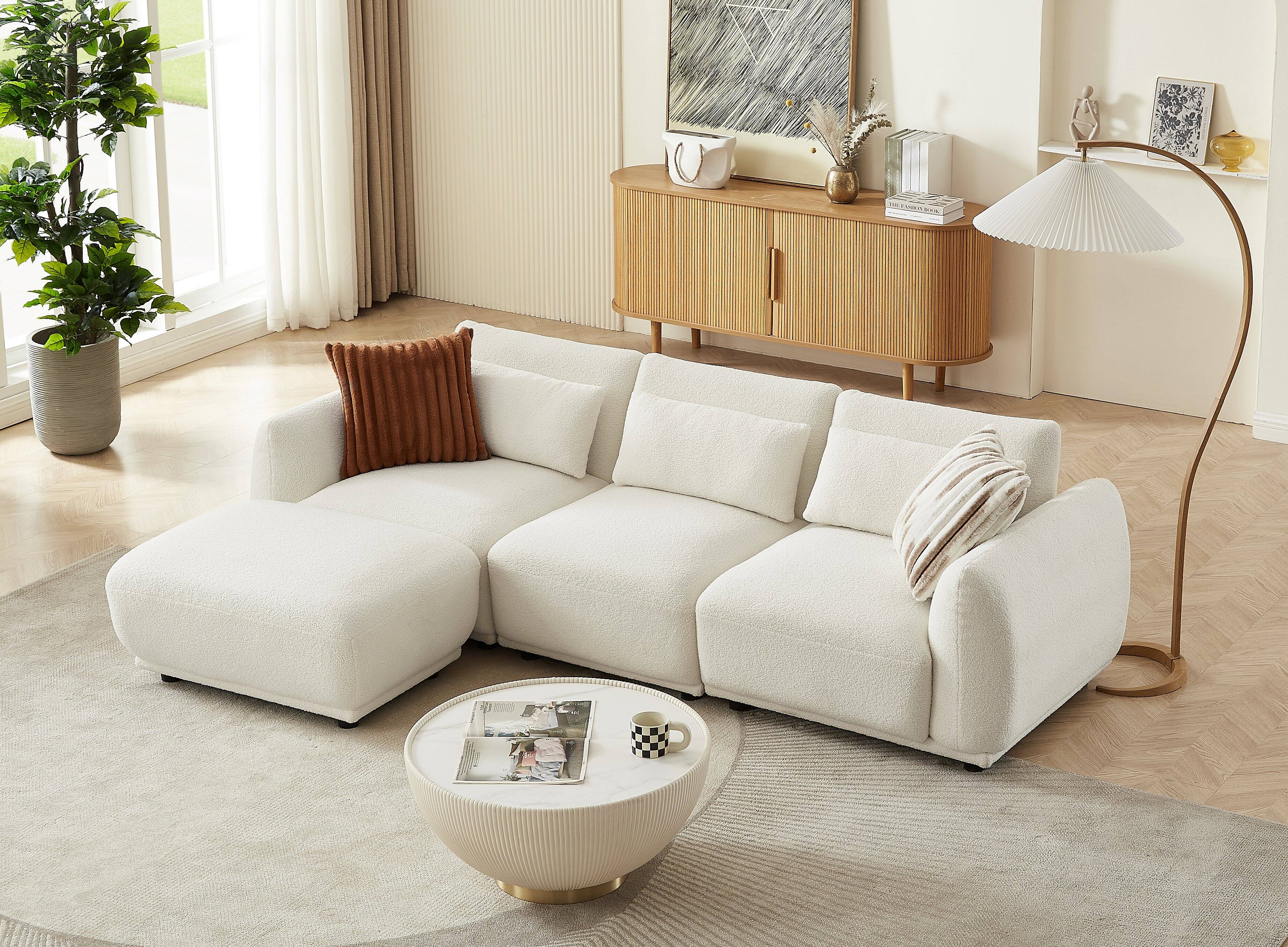 The image does not contain any text. It shows a modern living room with a white sofa, a round coffee table, a wooden sideboard, a floor lamp, and various decorative items.