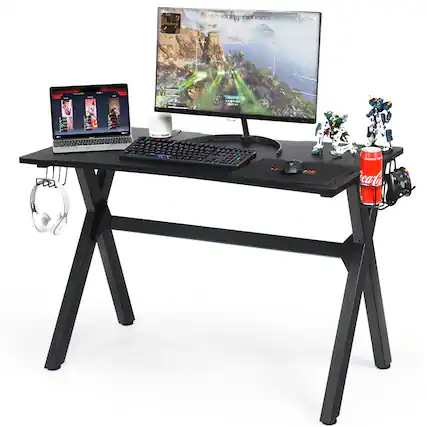 The image features a computer desk with a laptop, keyboard, and mouse on it. There is also a monitor and a pair of headphones. Additionally, there are two action figures and a can of soda on the desk.