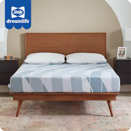 Sealy DreamLife is a bed that is designed to provide a comfortable and restful sleeping environment. The bed features a wooden headboard and a wooden footboard, which add a touch of elegance and sophistication to the room. The bed is covered with a blue and white striped comforter, which adds a pop of color to the space. The bed is also equipped with a wooden slatted bed frame, which provides additional support and stability. The combination of these elements creates a cozy and inviting atmosphere that is perfect for relaxation and rejuvenation.