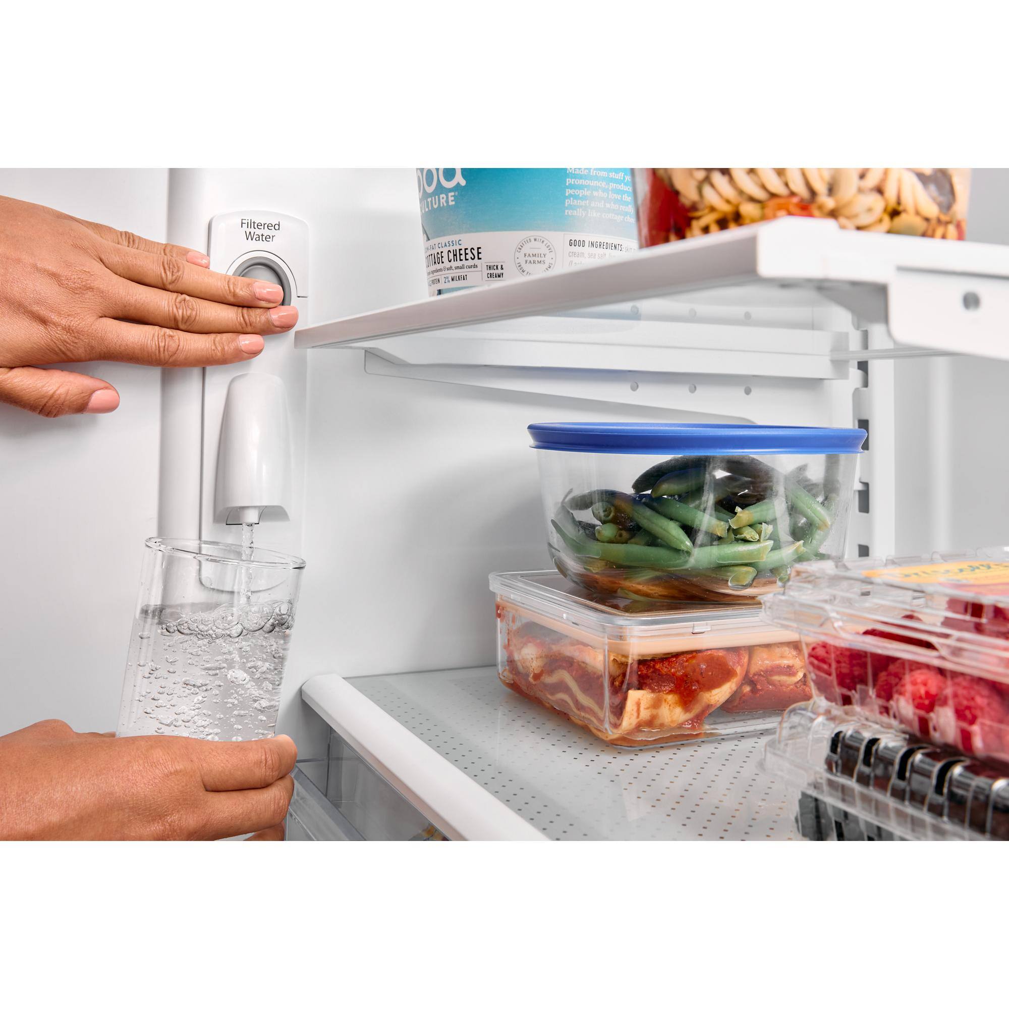 The image shows a refrigerator with a variety of food items inside. There are several bottles, including one of water, and a container of green beans. The refrigerator is stocked with a variety of foods, including meat and vegetables. The person in the image is reaching for a bottle of water, which is located on the top shelf of the refrigerator. The refrigerator is filled with food items, making it a well-stocked and convenient place for meal preparation.