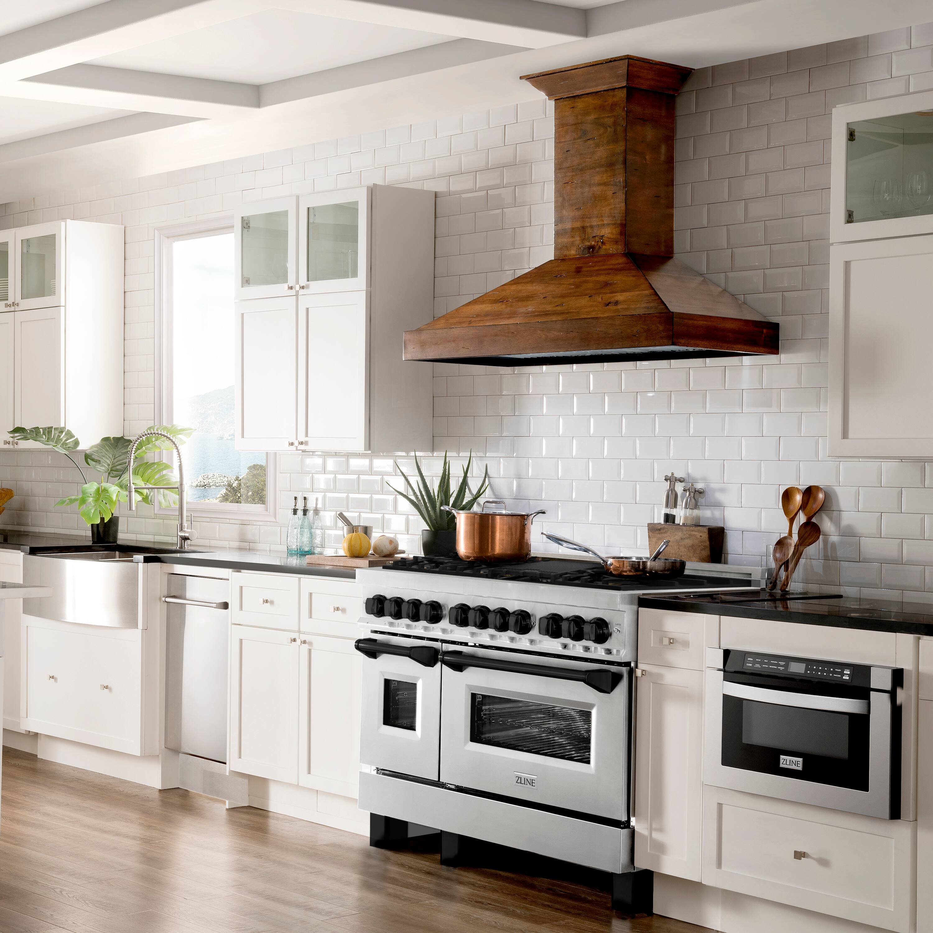 The image features a large, clean, and well-organized kitchen with white cabinets and a black stove. The kitchen is equipped with a sink, oven, and stove, and there are various items on the countertops, such as a bowl, a spoon, and a potted plant. The kitchen also has a window, allowing natural light to enter the space. The overall atmosphere of the kitchen is bright and inviting, making it an ideal space for cooking and entertaining.