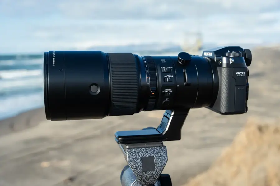 The image features a large camera lens, specifically a Fujinon lens, which is mounted on a tripod. The lens is set up on a beach, capturing the beautiful ocean view. The camera is positioned to capture the perfect shot, with the lens pointed towards the ocean. The tripod provides stability and allows the photographer to focus on their subject without worrying about camera shake.