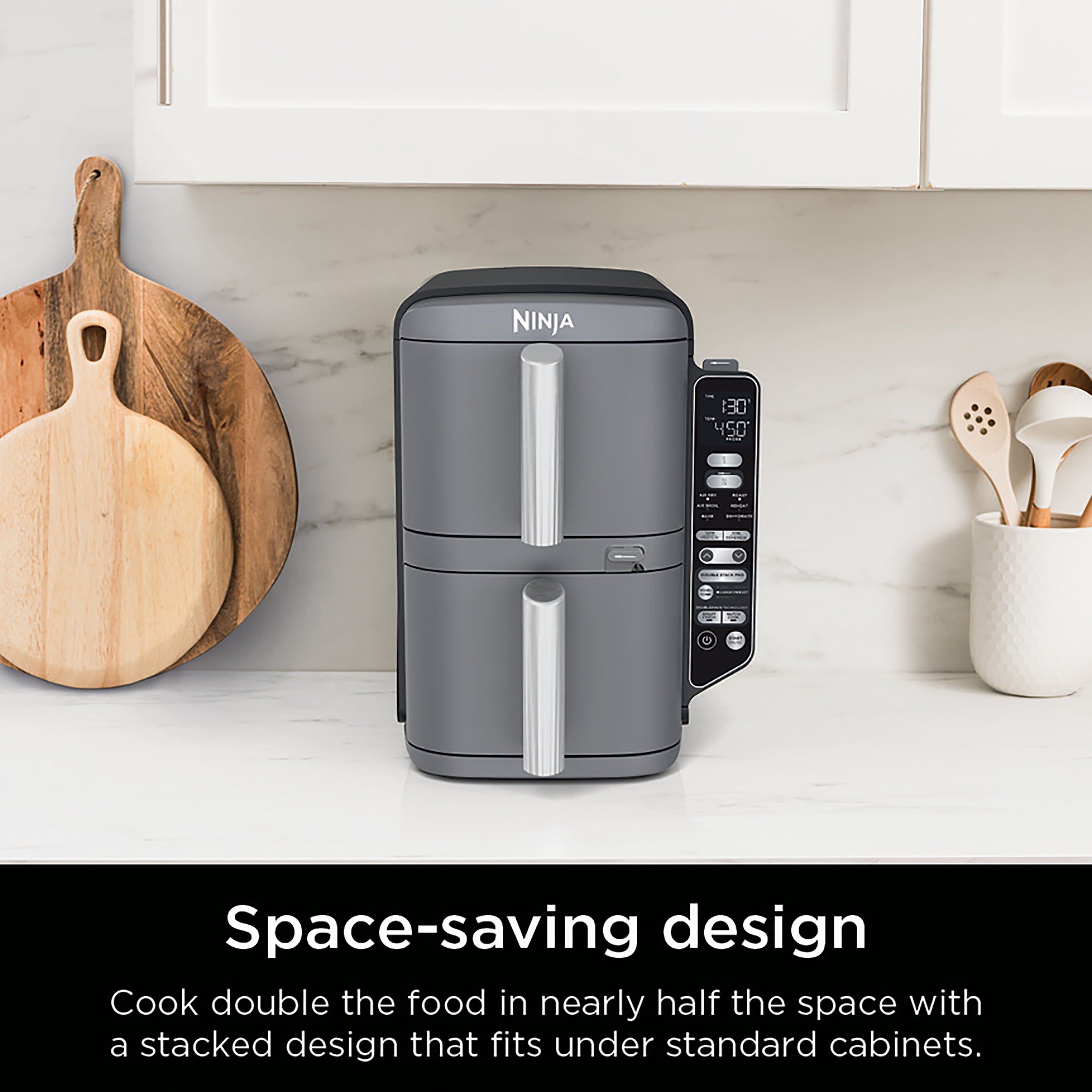 The image features a Ninja 130 450 space-saving design, which is a compact appliance that allows you to cook double the food in nearly half the space. It fits under standard cabinets, making it a practical and efficient choice for small kitchens. The appliance is placed on a countertop, surrounded by various kitchen utensils such as spoons, a bowl, and a knife. The image emphasizes the space-saving design of the Ninja 130 450, making it an ideal choice for those with limited kitchen space.