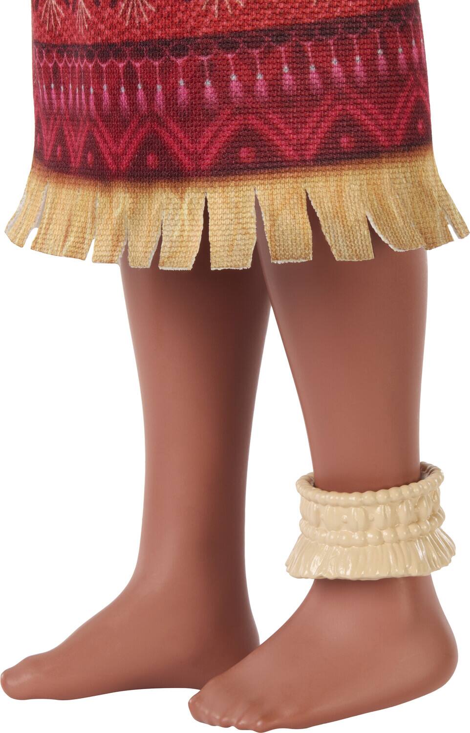 The image shows a close-up of a person's lower legs and feet. They are wearing a red skirt with a patterned design and fringed edges. Additionally, they have a cream-colored woven anklet on one ankle.