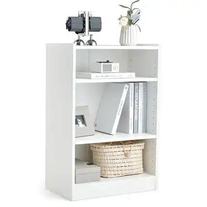 The image features a white bookshelf with various items on it. There are several books placed on the shelf, with one book being larger than the others. Additionally, there is a vase on the shelf, and a basket is placed on the bottom shelf. The bookshelf is situated next to a white wall, and there is a potted plant nearby. The arrangement of the items on the shelf creates an organized and visually appealing display.