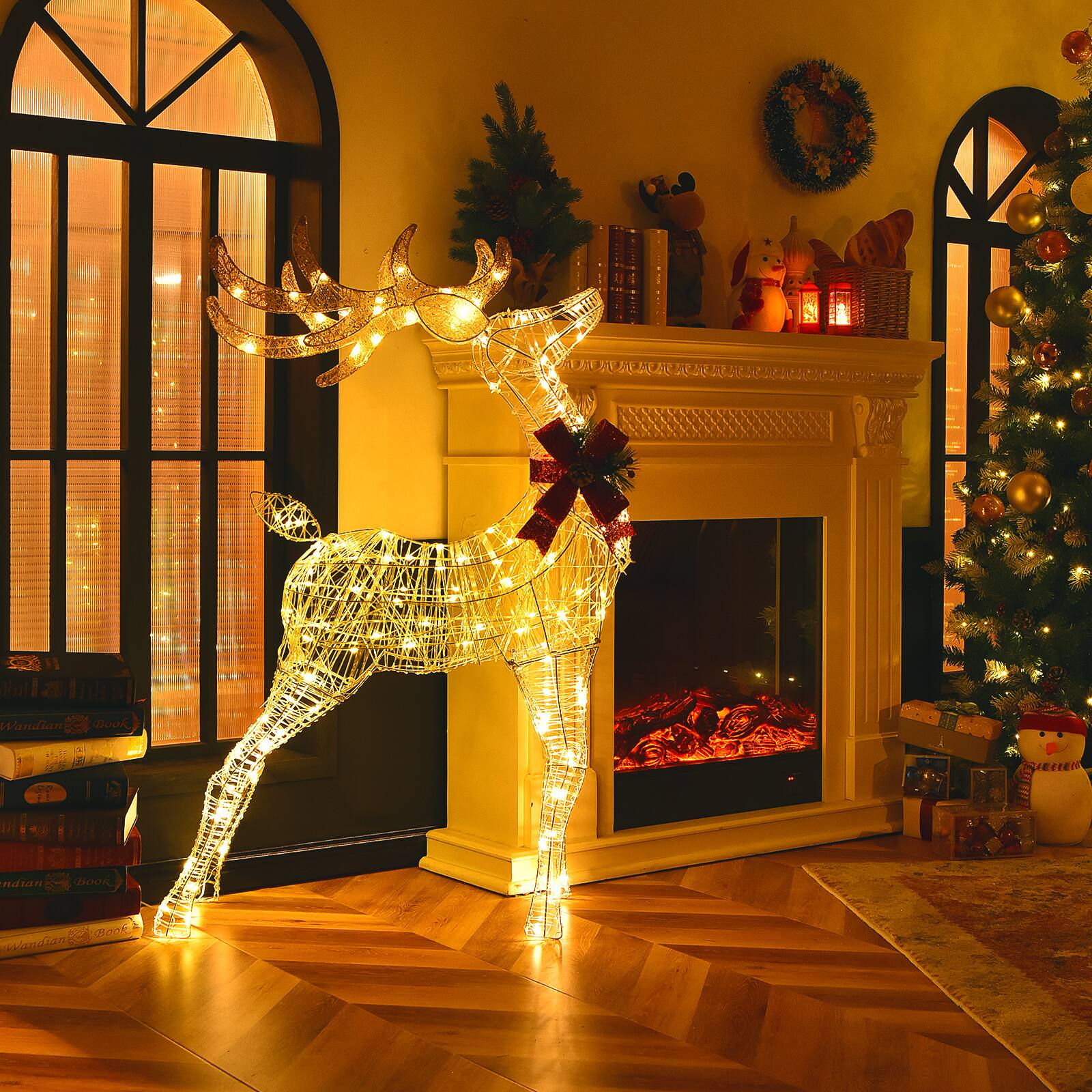 A lit up reindeer decoration is standing in front of a fireplace.