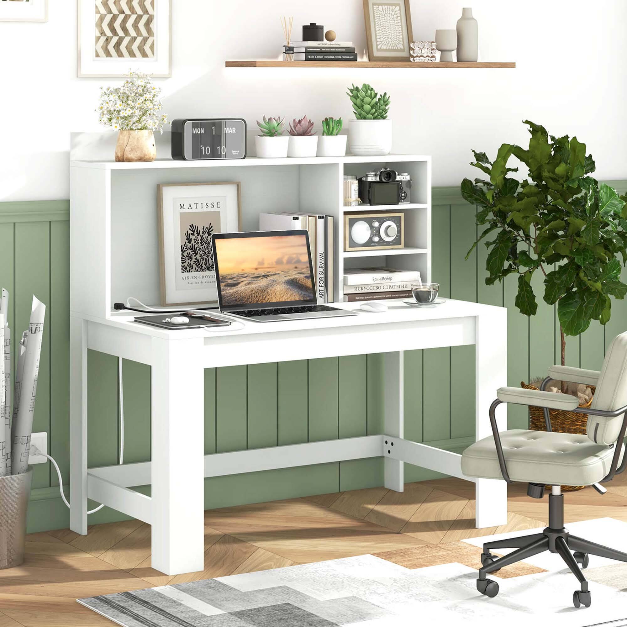 The image shows a small white desk with a laptop, a keyboard, and a mouse on it. The desk is situated in a room with a green wall and a shelf above it. There are several books scattered around the desk, and a potted plant is placed nearby. Additionally, there are two cups on the desk, and a chair is positioned in front of the desk. The scene appears to be a cozy workspace, possibly in a home office or a bedroom.
