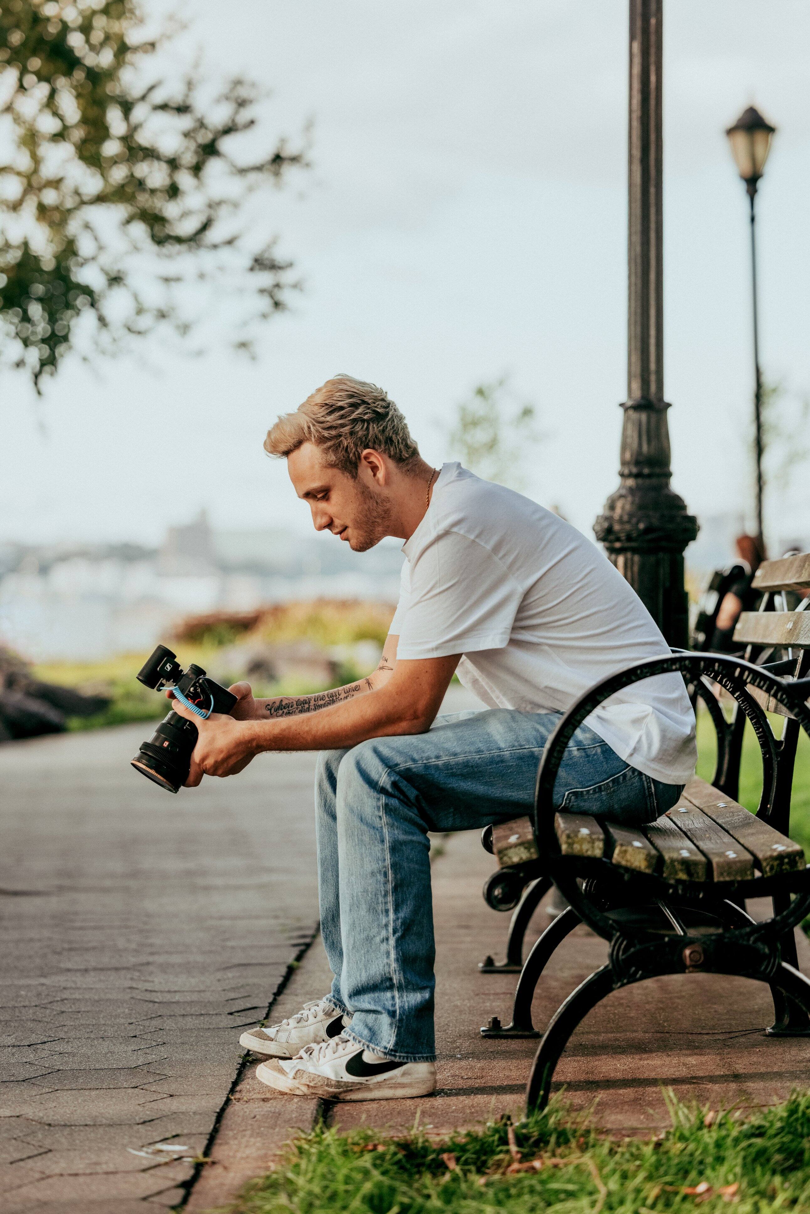 The man is sitting on a bench, holding a camera.