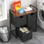 The image features a laundry room with a washing machine and a dryer. There is a small table with a basket and a few items on it, including a bottle of detergent. The table is located near a window, and there is a trash can nearby. The laundry room also has a shelf with a few items on it, such as a towel and a book.
