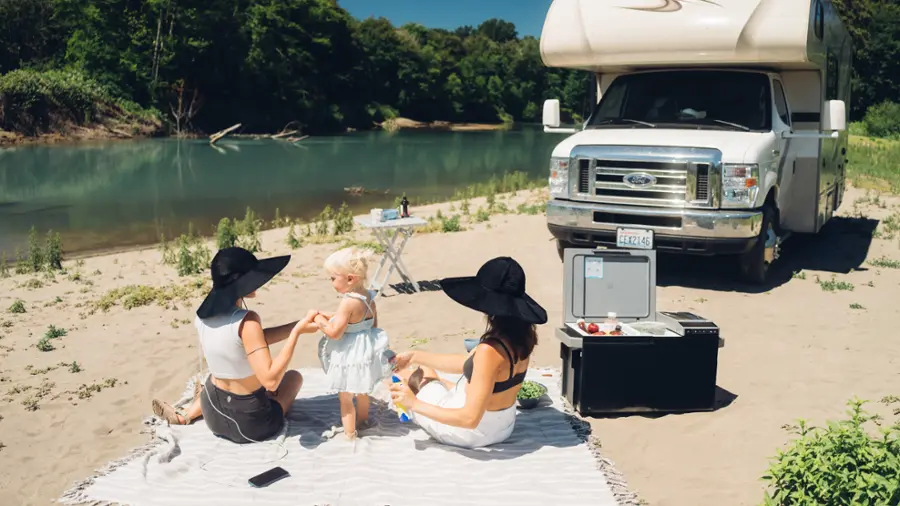 I cannot group or correct the text as it does not appear to be related to the image. The image shows a group of people, including a woman and a child, sitting on a blanket on a beach. There is also a truck parked nearby.