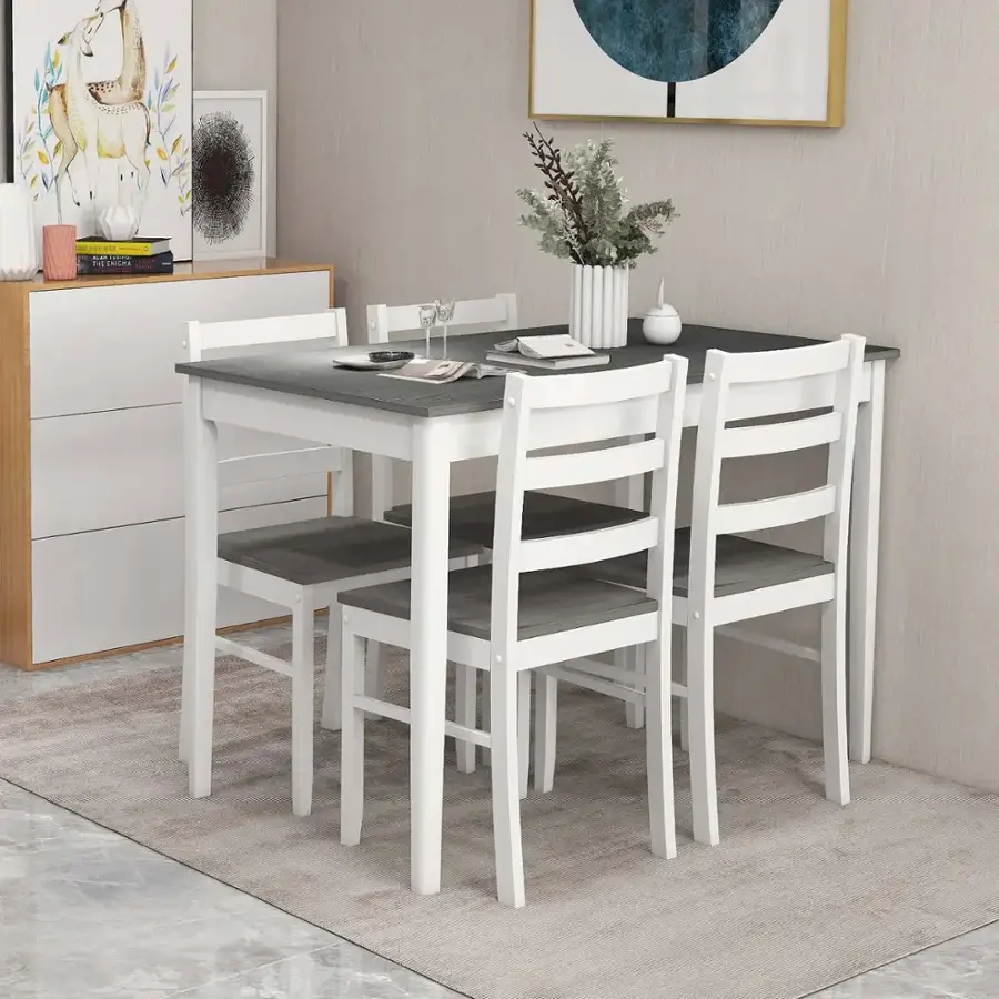 The image shows a white dining table with four white chairs arranged around it. The table is set with a vase of flowers and a bowl of fruit, creating a pleasant and inviting atmosphere. The chairs are positioned in a way that allows for easy conversation and enjoyment of the meal. The table is situated in a room with a white rug, adding to the overall clean and elegant appearance of the space.