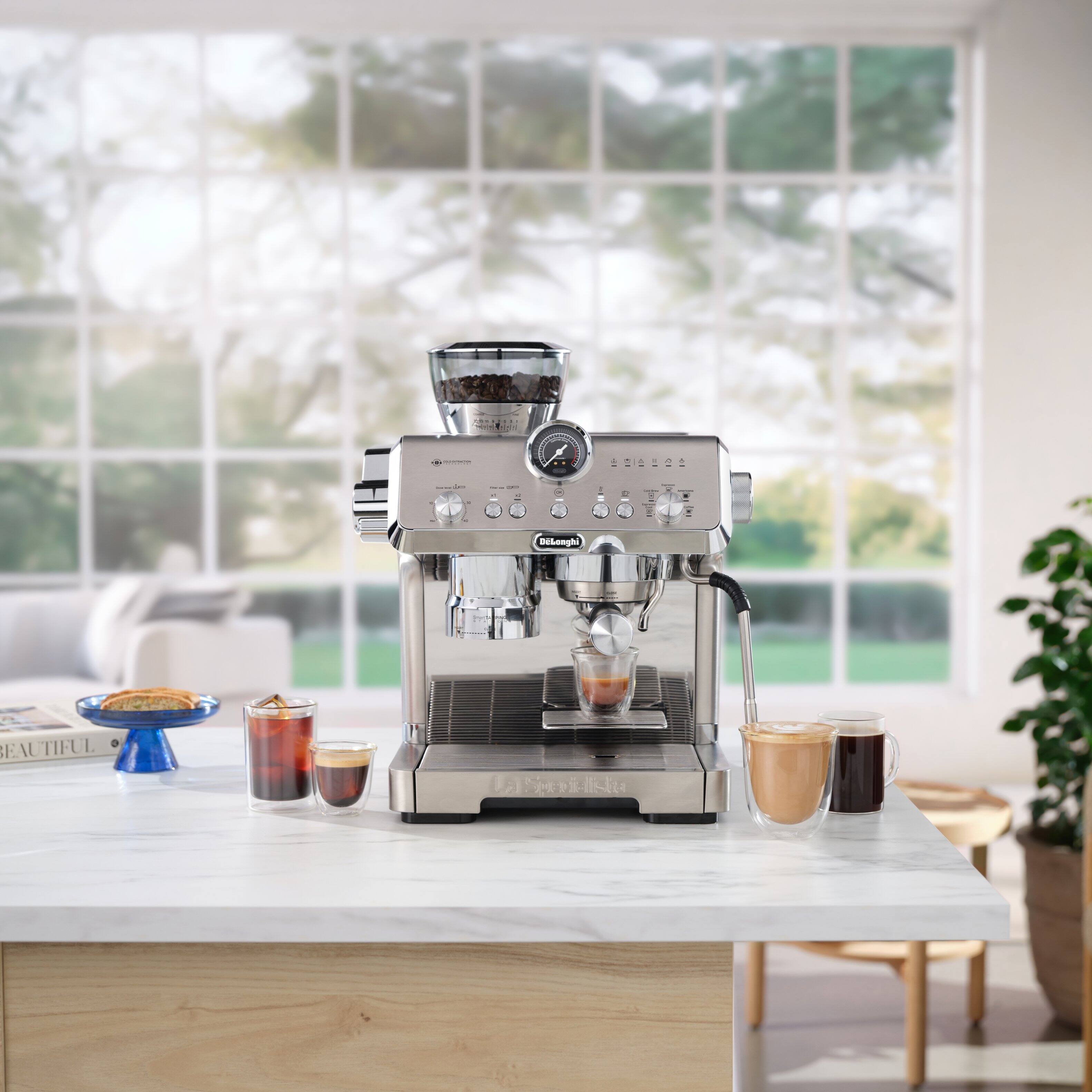 "A beautiful Dilonghi espresso machine is on a counter with a window view in the background."