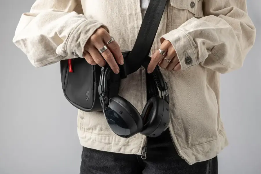A person is holding a black strap and a pair of headphones.
