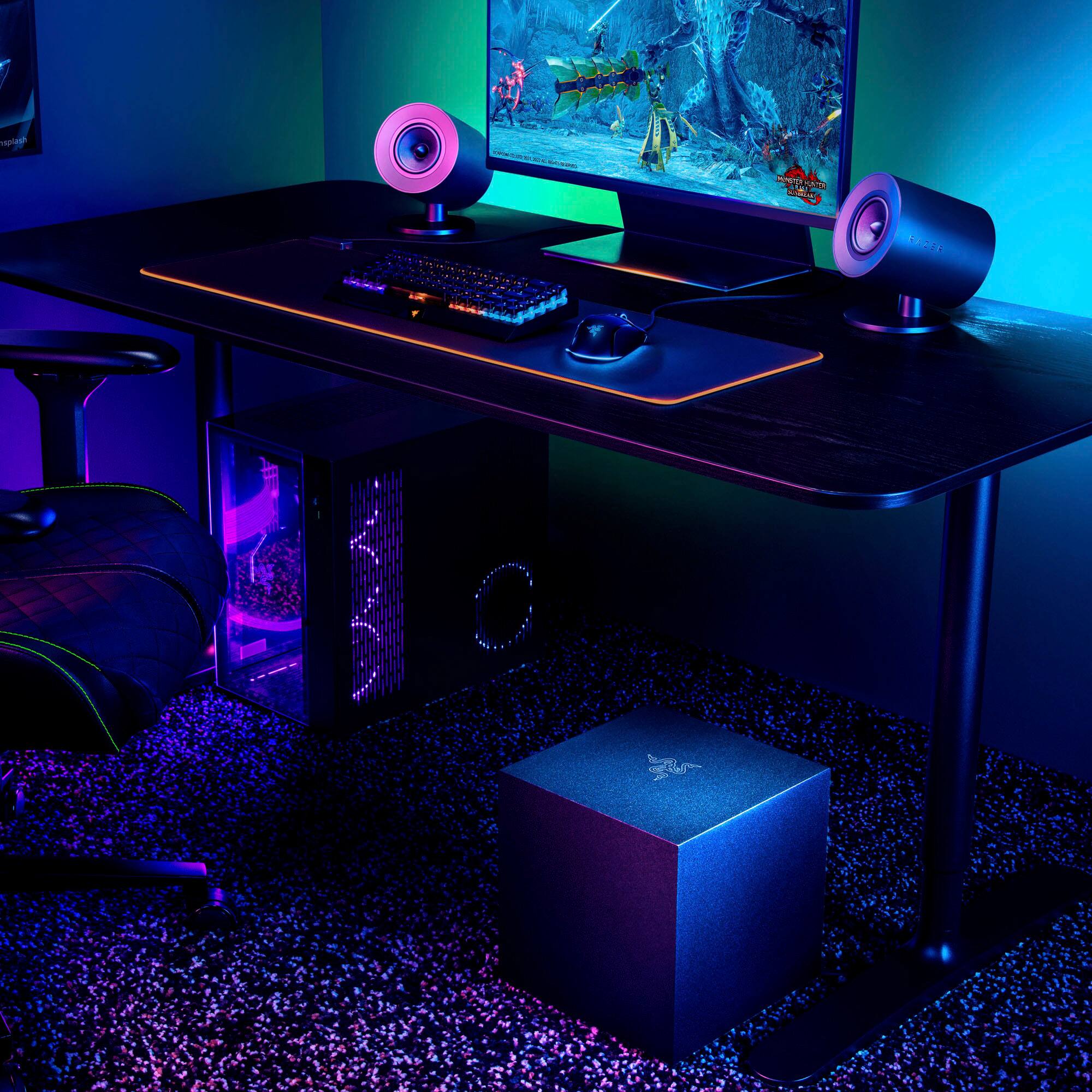 The image features a computer desk with a monitor, keyboard, and mouse. There is also a chair positioned in front of the desk. The desk is set up in a dark room, creating a focused atmosphere for work or gaming.