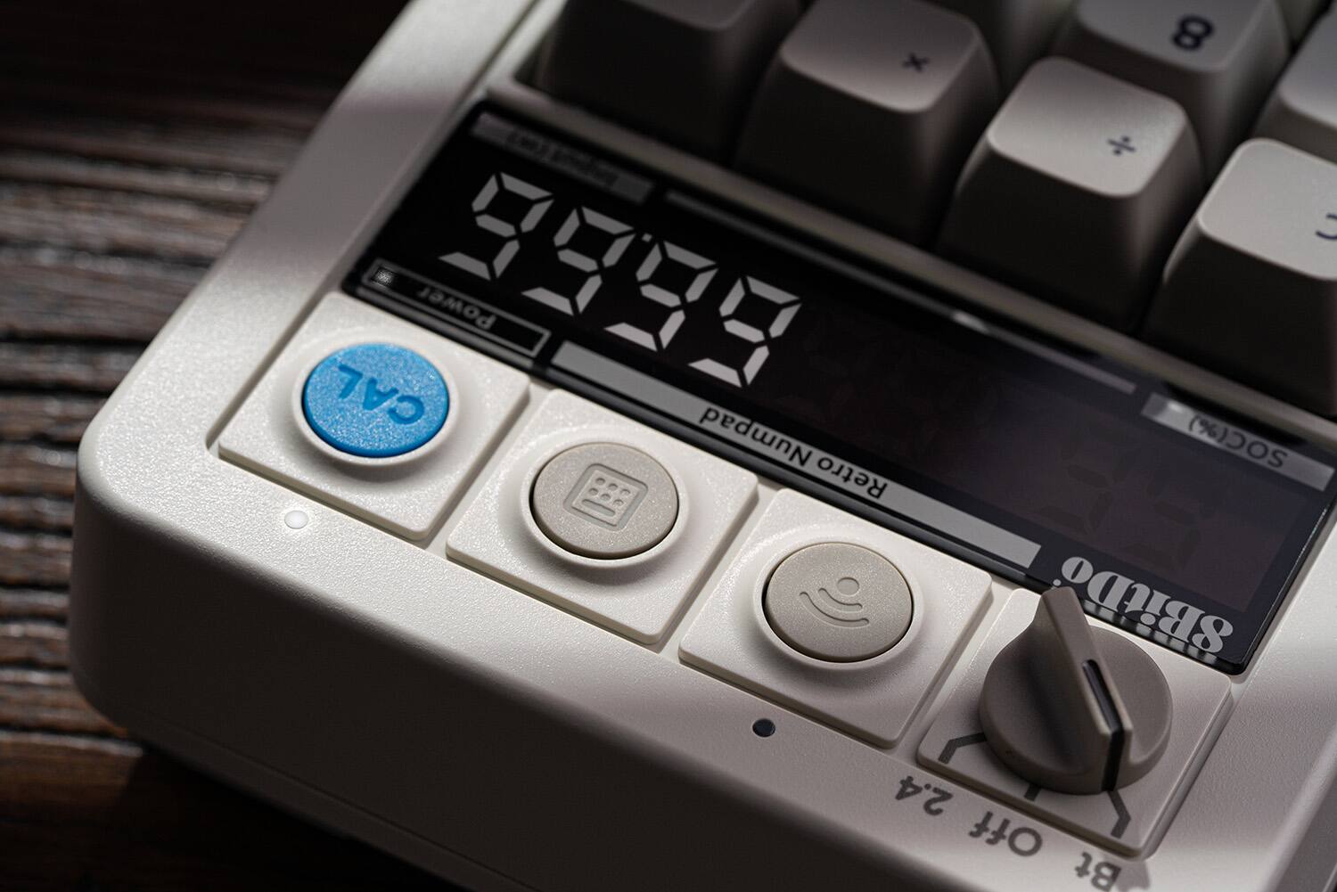 The text on the image reads "x - 9999 Power CAL Numpad Retro 8 SOC(%) SBitDo 2.4 Off Bt." This text is likely related to the electronic device, possibly providing information about its features or functions.