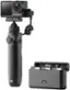 The image features a DJI Osmo camera with a black handle and a silver body. The camera is attached to a tripod, and it is positioned in front of a grey box. The camera is equipped with a green lens, and it is ready for use.