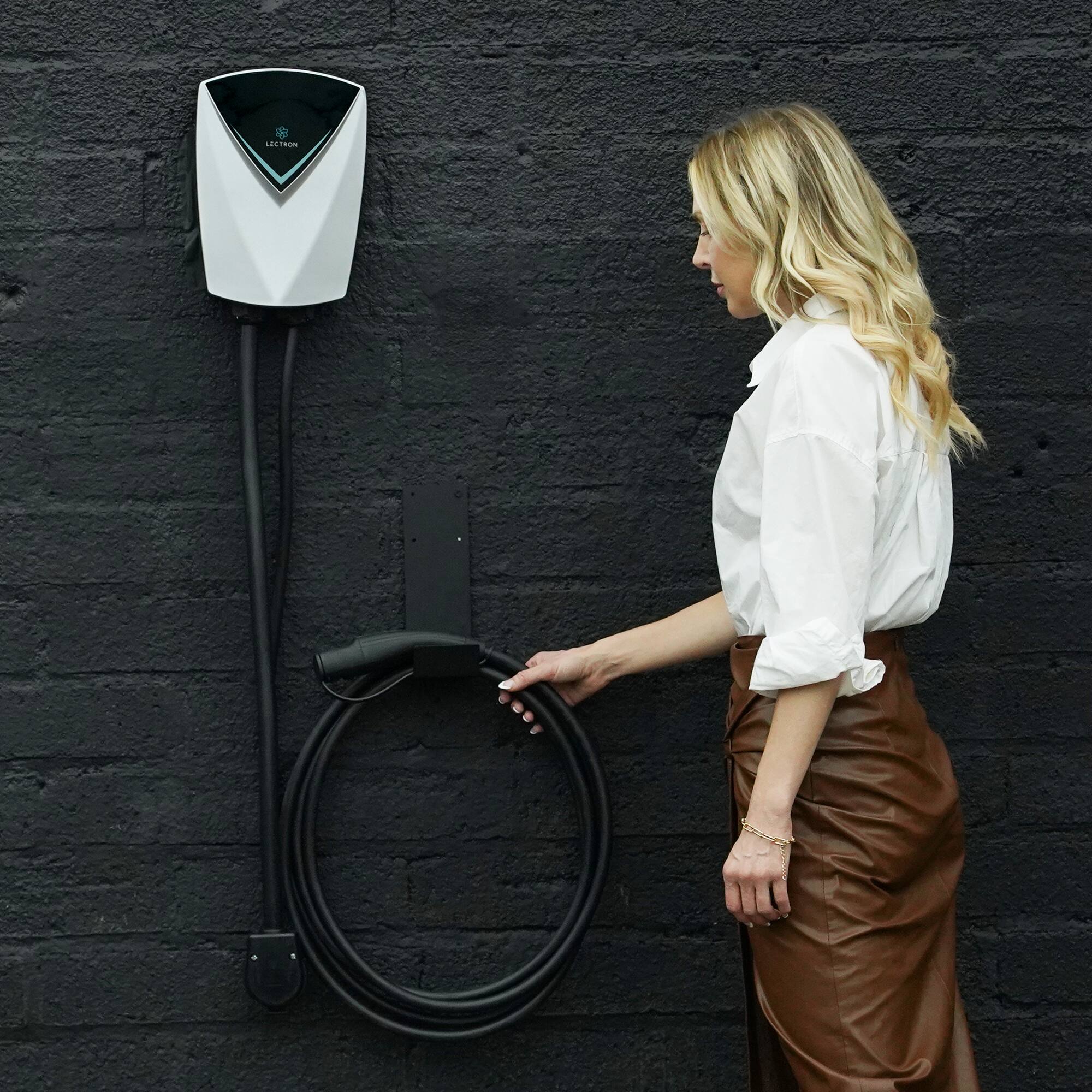 I'm sorry, but I cannot group or correct the text "LEETEIN" as it does not appear to be related to the image. The image shows a woman standing next to a brick wall, holding a cord or a charger.