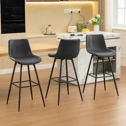 1. The image shows a modern kitchen with a marble countertop and three black bar stools.
2. On the countertop, there is a green toaster, a bowl of lemons, a vase with white flowers, and a cookbook.
3. The kitchen features a built-in oven, a coffee maker, and a window with curtains.
4. The floor is made of light wood, and the overall color scheme is neutral with beige walls.