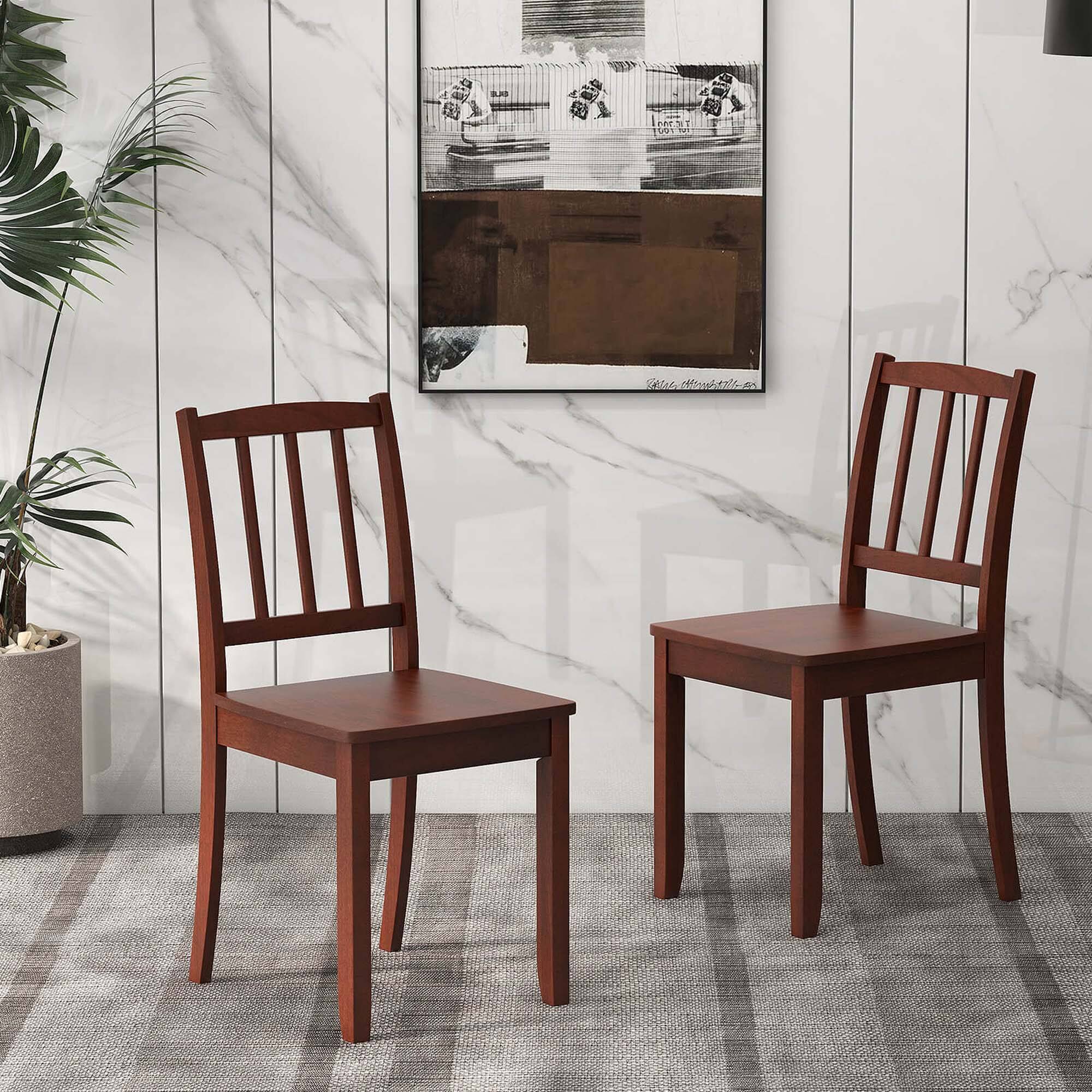 The image shows a living room with two wooden chairs placed in front of a picture. The chairs are positioned on a carpeted floor, and there is a potted plant nearby. The picture is hanging on the wall, adding a decorative touch to the room. The arrangement of the chairs and the picture creates a cozy and inviting atmosphere in the living room.