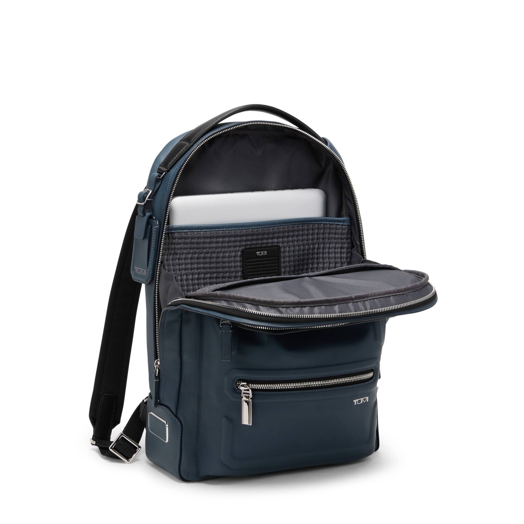 The image shows a navy blue backpack with multiple compartments. The main compartment is open, revealing a padded laptop sleeve. There is a smaller front pocket with a zipper, and a mesh pocket on the inside of the lid. The backpack has a black shoulder strap and a handle on top.