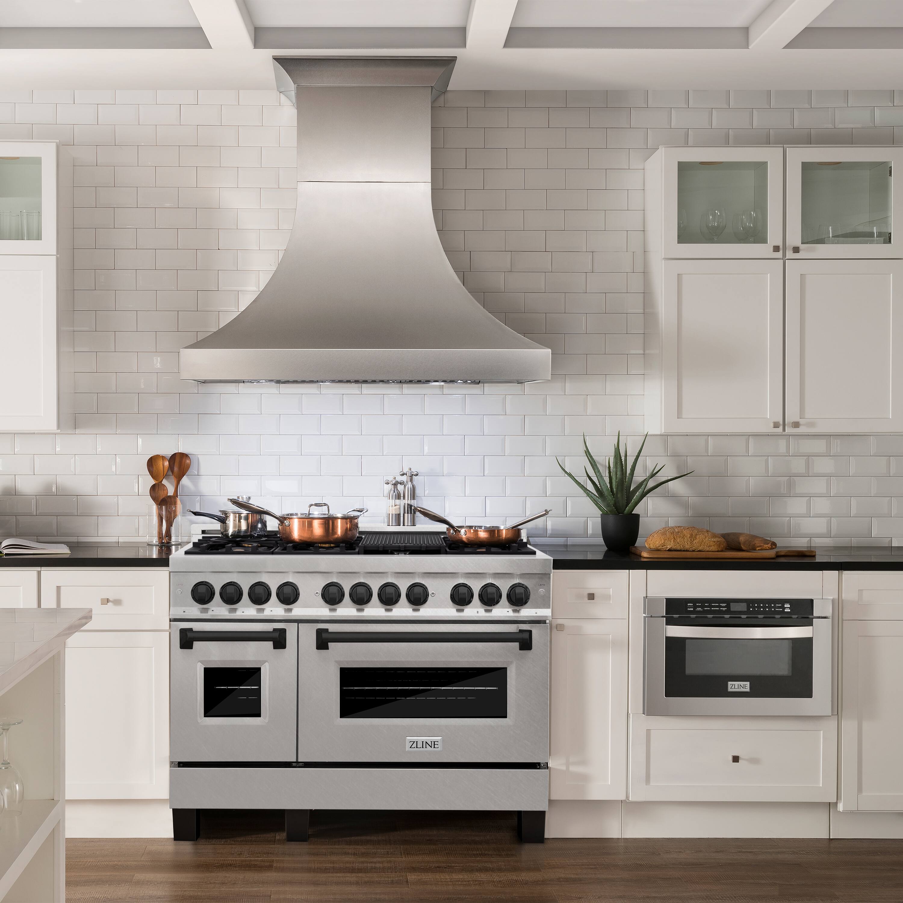 The image shows a kitchen with a stainless steel stove top oven and a vent hood. The oven is positioned under the vent hood, which is located above the stove. The kitchen also features white cabinets and a tile backsplash. Additionally, there is a potted plant and a few bottles in the scene.