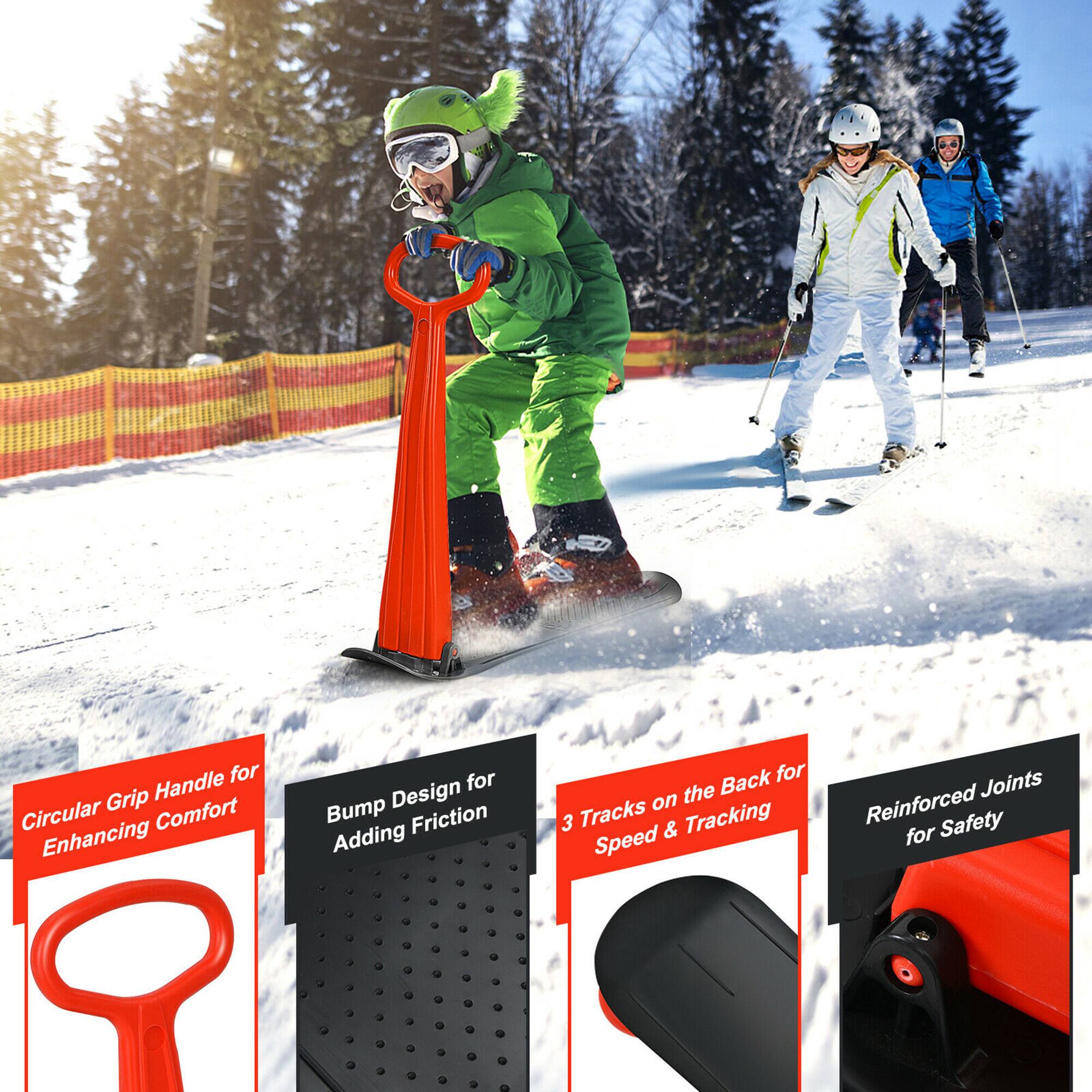 The image features a snowy slope with a person wearing a green snowsuit and riding a snowboard. The person is holding a red handle, which is likely a part of a snowboarding safety device. The image also shows a red and black snowboard, and a pair of skis can be seen in the background. The scene suggests that the person is enjoying a winter sport activity, possibly skiing or snowboarding, while wearing appropriate safety gear.