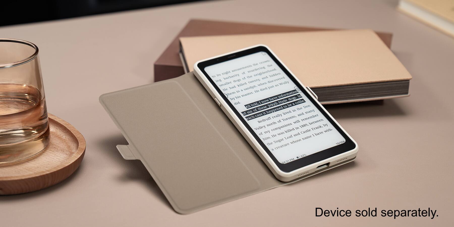 The image shows a cell phone placed on top of a book, with a glass of alcohol nearby. The text on the image reads: "Device sold separately."