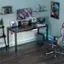 The image features a computer desk with a chair, a keyboard, and a mouse. There are also two monitors on the desk, and a laptop is placed nearby. In addition to the computer equipment, there are several books scattered around the desk, and a potted plant is located to the left of the desk. A TV is mounted on the wall above the desk, and a cell phone can be seen on the desk as well. The room also contains a bed, which is situated to the right of the desk.