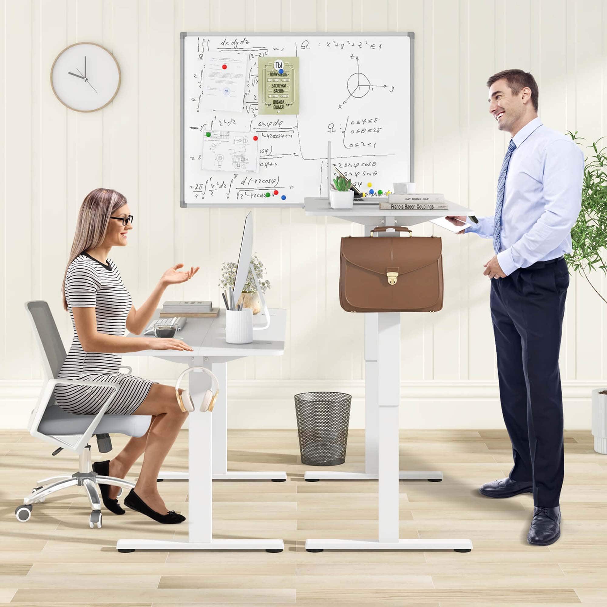 The image shows a man and a woman in a room. The man is holding a briefcase and standing next to a woman who is sitting at a desk. The desk has a laptop, a keyboard, and a clock on it. There is also a potted plant in the room, and a handbag is placed on the floor. The man is wearing a tie, and the woman is wearing glasses. The scene suggests a professional or work-related setting.