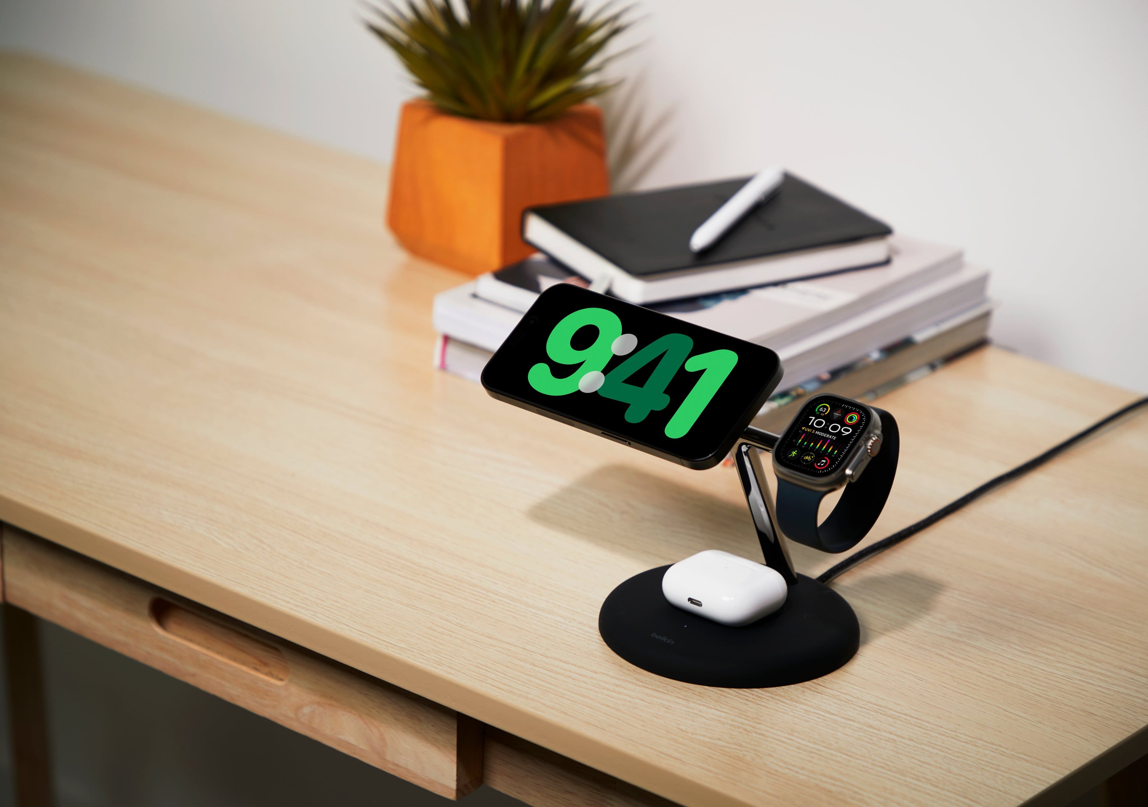 The image shows a desk with a digital clock displaying the time of 9:41. The clock is placed on a black stand, and there are several books scattered around the desk. The scene appears to be a typical workspace or study area.