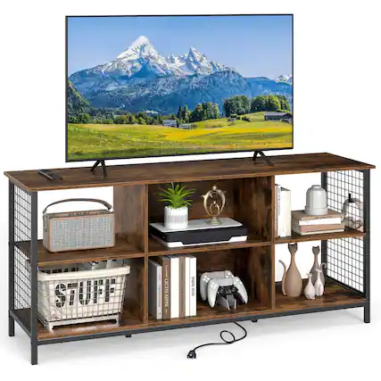 I have a large flat screen TV on top of a wooden stand. The stand also has a shelf with various items, including books, a potted plant, and a vase. There is a remote control on the shelf, and a basket is placed on the stand. The overall scene is a cozy and organized living space.