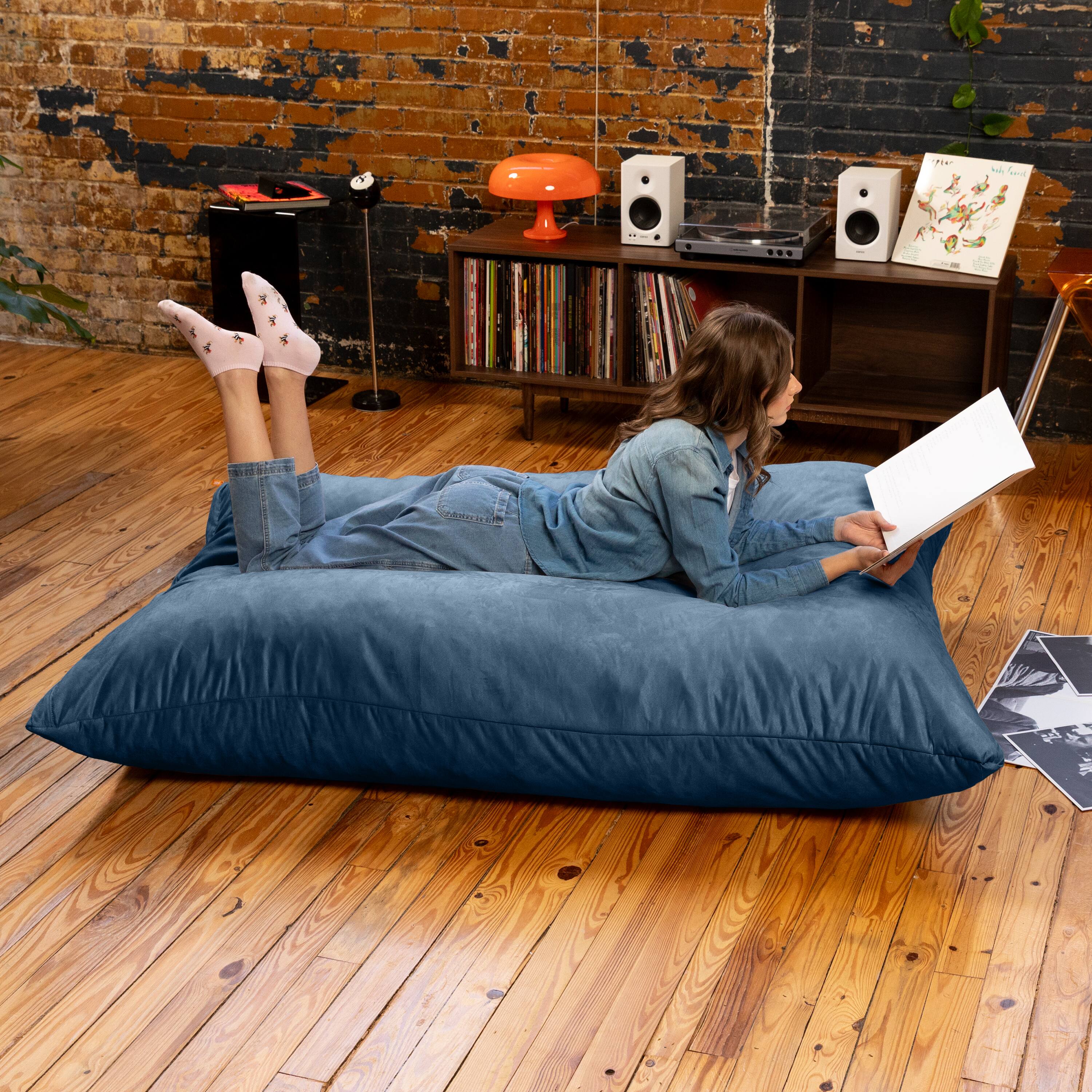 The text in the image is not clearly visible or legible. However, based on the context, it appears to be a promotional or descriptive text related to the product being advertised, which is a large, plush bean bag. The text might include details about the product's features, materials, or brand information. If you have specific text you need help with, please provide it, and I can assist in correcting or clarifying it.