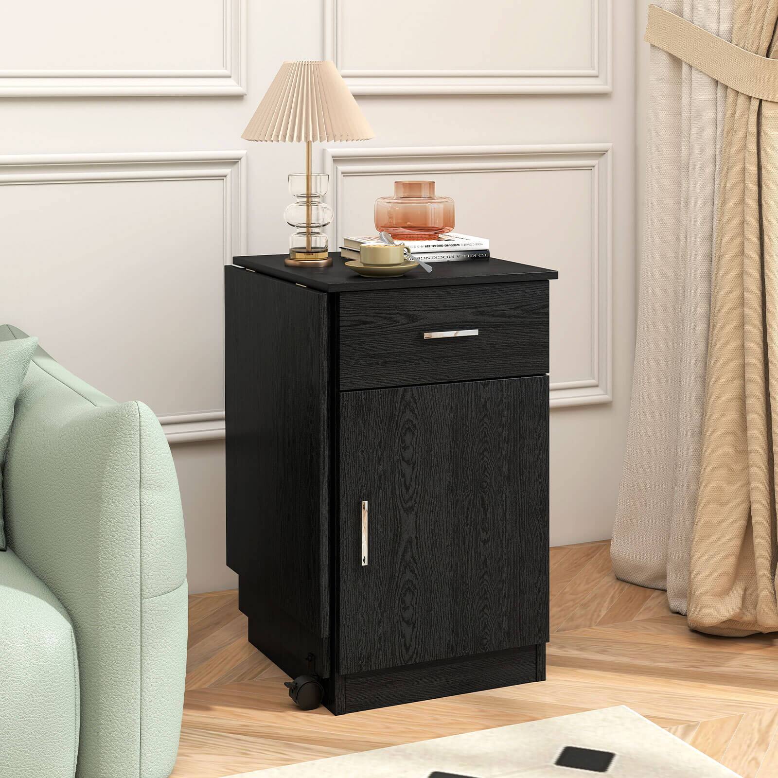 The image shows a small black table with a lamp on top of it. The table is placed in front of a chair, and there is a curtain nearby. The table has a drawer, and it is situated in a living room.