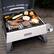 Cuisinart NOVA S grill is filled with a variety of food items, including hot dogs, hamburgers, and vegetables such as carrots and zucchini. The grill is placed on a wooden deck, and the food is arranged in an appetizing manner. The grill is designed to cook food evenly and efficiently, making it a popular choice for outdoor cooking enthusiasts.