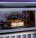 The image shows a microwave with a dish of food inside. The microwave has a 2.2 cu. ft. capacity, and there is a button to push for heating the food. The dish appears to be a casserole, and the microwave is open, revealing the food inside.