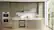 The image shows a large kitchen with a center island and a window above it. The kitchen is equipped with a stove, oven, and sink, and features a variety of cabinets and drawers. There are several items on the countertop, including a vase, a knife, a spoon, and a bottle. The kitchen also has a potted plant and a bowl, adding to the overall ambiance of the space.