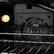 The text "HLLLE CON TEVUE" is not related to the image. The image shows a close-up view of a black oven with a light on, and the oven door is open.