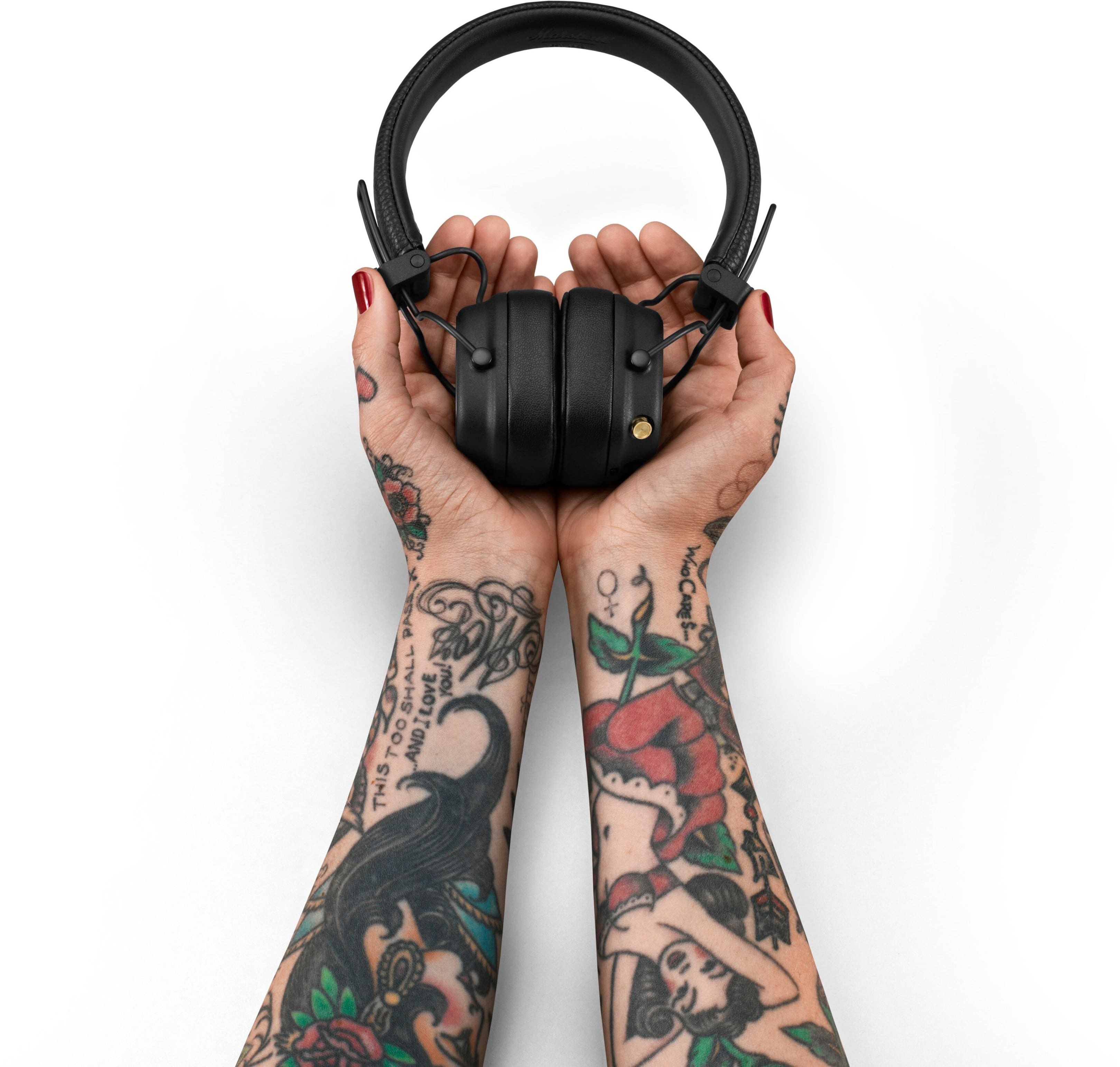 This is a tattooed arm holding a pair of headphones. The tattooed arm is wearing red nail polish.
