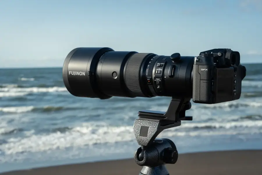 The image features a large camera lens, specifically a Fujinon lens, set up on a tripod near the ocean. The lens is positioned to capture the beautiful ocean view, and it is likely being used for photography or filming purposes. The tripod provides stability and support for the lens, ensuring that it remains in place and focused on the subject.