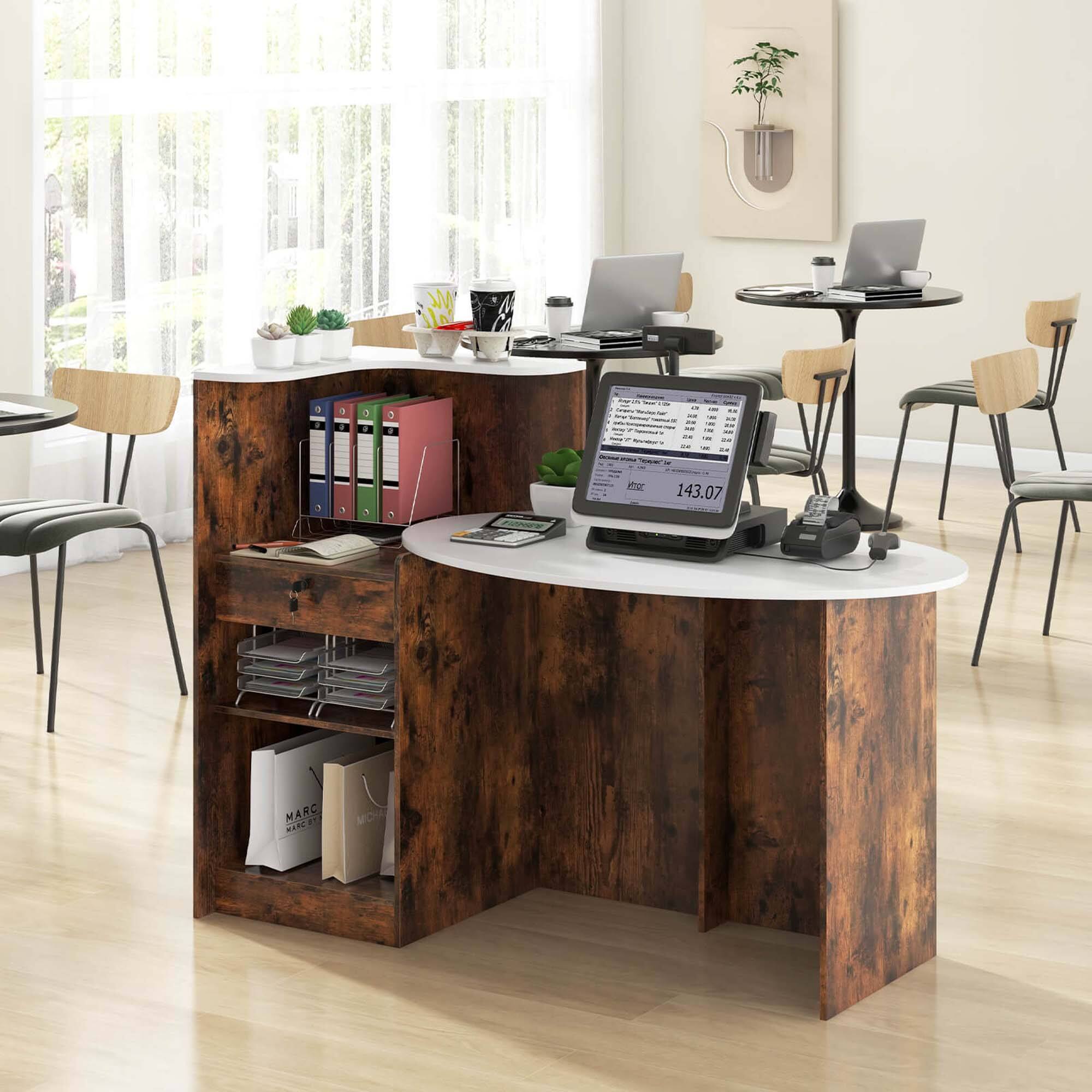 The image shows a room with a wooden desk that has a laptop, a mouse, and a keyboard on it. There are also several books and a cup placed on the desk. The room also contains a dining table with chairs around it. In addition, there is a potted plant in the room, and a TV is mounted on the wall. The room appears to be a workspace or a home office.