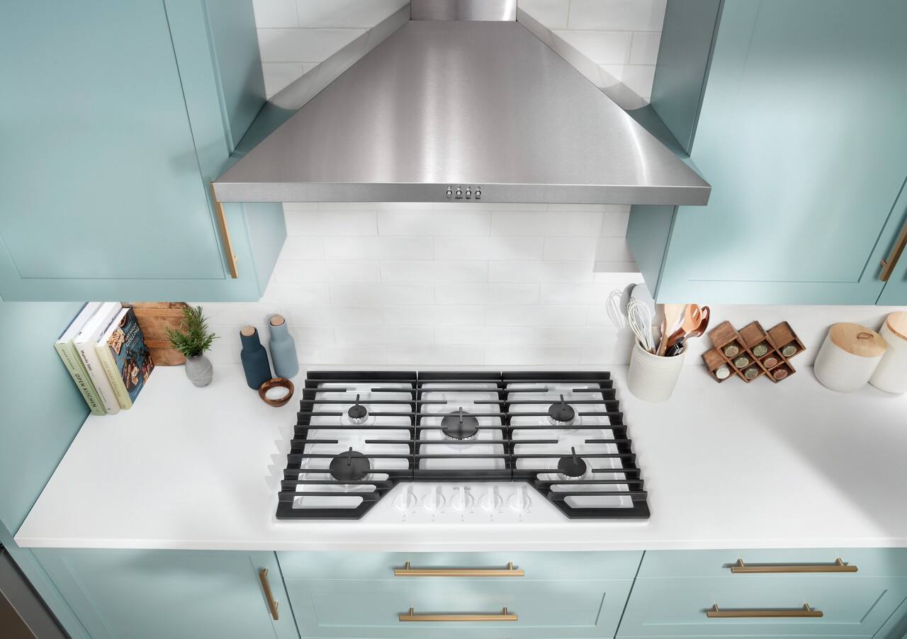 The image features a kitchen with a stove top oven and a vent hood. The stove has a black and white design, and there are several books placed on the countertop. Additionally, there are various items on the counter, including a potted plant, a vase, a cup, and a bowl. The kitchen appears clean and well-organized, with the stove being the main focal point.