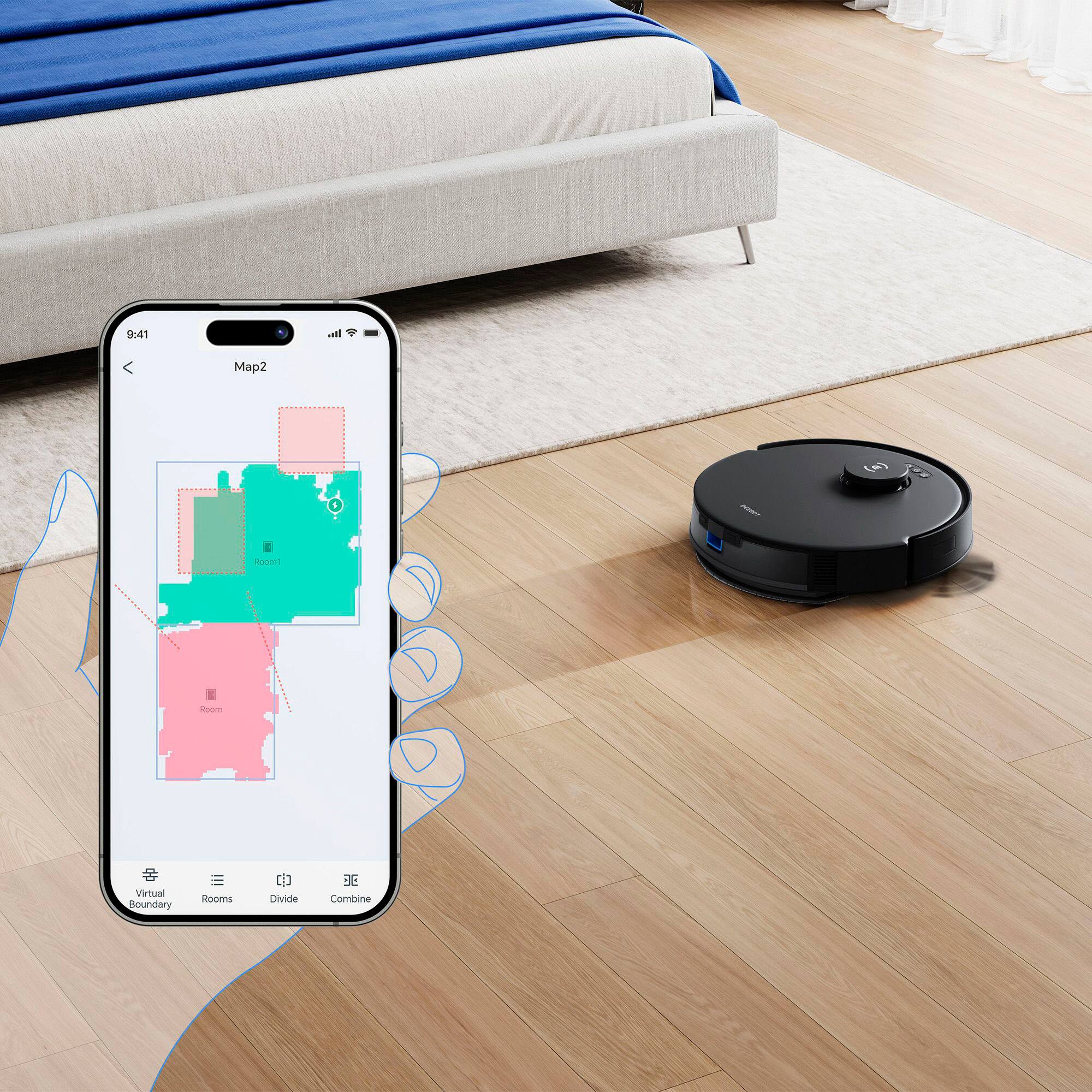 The image shows a person holding a cell phone with a map of a room displayed on the screen. The map is divided into different sections, including a bedroom, living room, and kitchen. The person is standing next to a robot vacuum cleaner, which is also present in the room. The cell phone is being used to guide the robot vacuum cleaner, ensuring that it cleans the room efficiently and effectively.