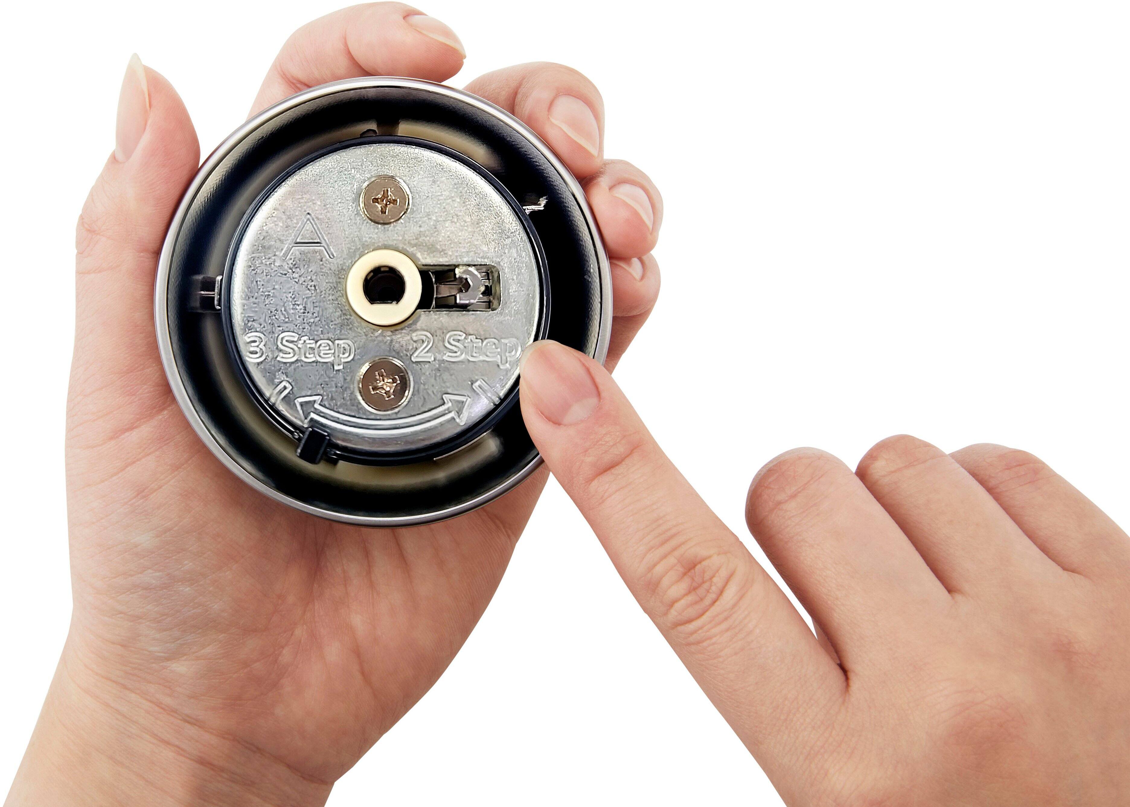 A person is holding a small object, possibly a watch or a small appliance, in their hands. The object has a dial or a knob, and the person is examining it closely. The hands are positioned in such a way that they are touching the object, and the fingers are pressing on it. The person is likely trying to understand the function or the mechanism of the object, as they are carefully inspecting it.