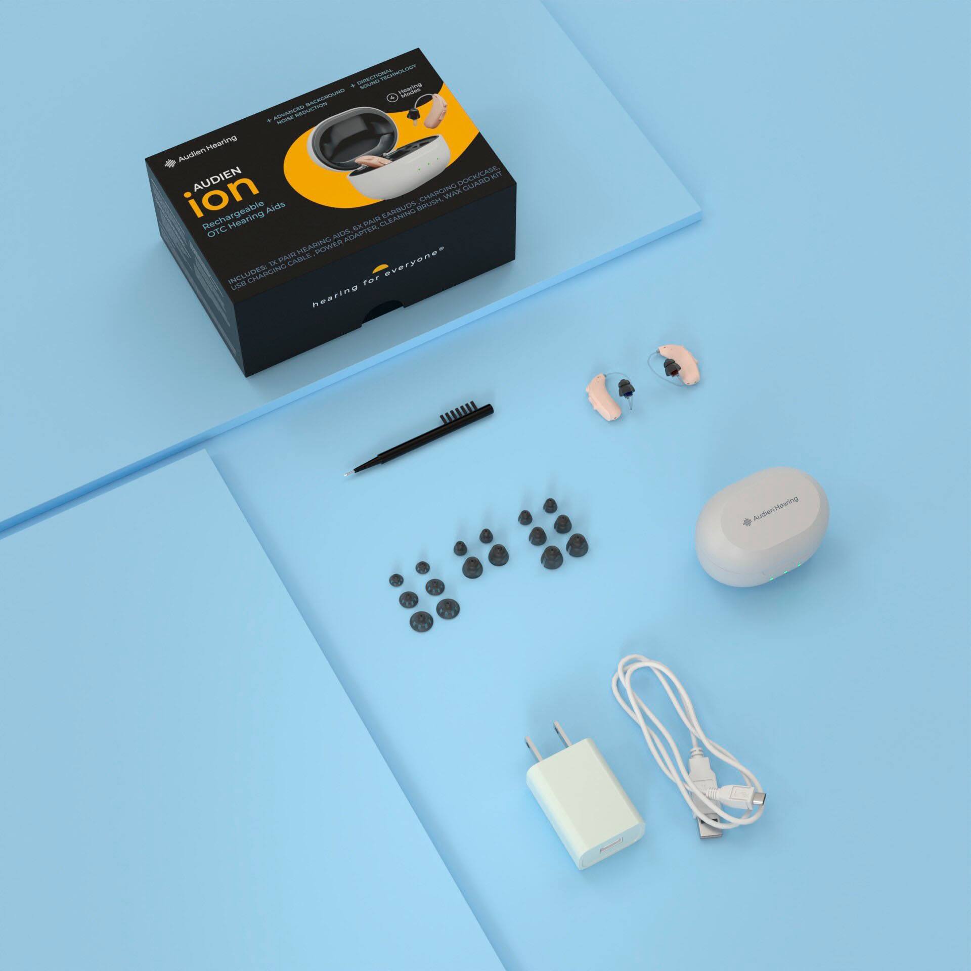 The image features a box containing a hearing aid, along with a charger and earbuds. The box is placed on a blue surface, and the items are laid out neatly. The text on the image reads "ION Hearing Audien," which suggests that the product is related to hearing aids and accessories.