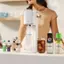 The image features a woman standing next to a counter with various items on it. There are several bottles, including a Pepsi Zero Sugar drink, and a SodaStream machine. The woman is holding a glass filled with a drink, possibly a cocktail. The scene suggests that she is preparing or enjoying a beverage using the SodaStream machine.