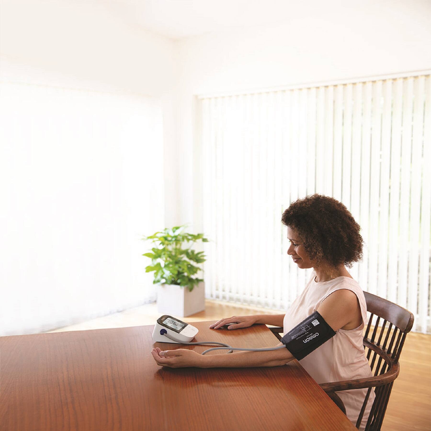 The text "178 omRon" is not related to the image. It seems to be an unrelated piece of information. The image shows a woman sitting at a table with a blood pressure monitor attached to her arm.