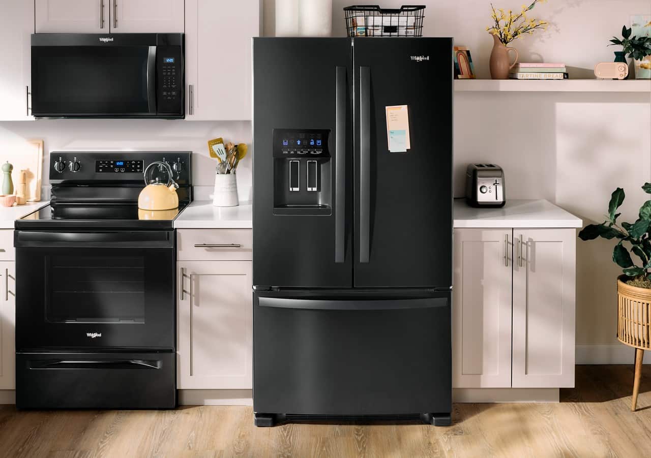 The image shows a kitchen with a black refrigerator, a stove, and a microwave. There is also a potted plant and a vase in the room. The refrigerator has a magnet on it, and there is a book on the counter. The kitchen is well-equipped with various appliances and decorative elements.