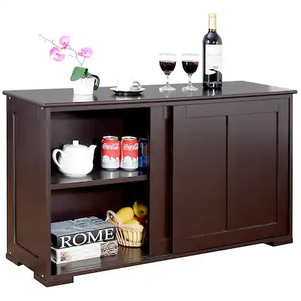 The image features a brown wooden cabinet with a shelf on top. On the shelf, there is a basket filled with fruit, including apples and oranges. Next to the fruit, there are two wine glasses, and a bottle of wine is placed nearby. Additionally, there is a vase with flowers, a cup, and a potted plant on the cabinet. The scene appears to be a cozy and inviting space for relaxation and enjoyment.